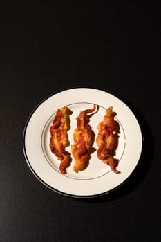 Three strips of cooked bacon on a white plate. Vertical shot.