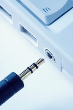 Black headphone wire connecting to a laptop computer. Vertical shot.