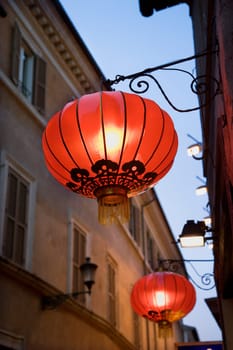 Low angle view of illuminated red paper lanterns hanging outside on a building facade. Vertical shot.