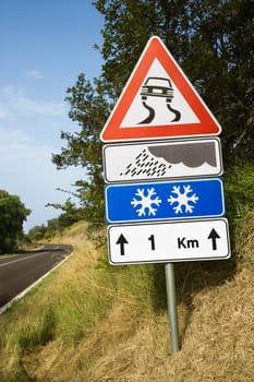 Signs warning of treacherous driving conditions on the side of a rural road. Vertical shot.