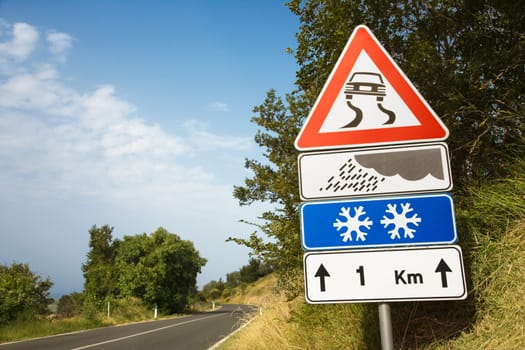 Low angle view of signs warning of treacherous driving conditions on the side of a rural road. Vertical shot.