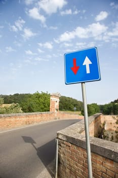 View of a rural road lined with a low brick wall.  In the foreground is a road sign with arrows. Vertical shot.