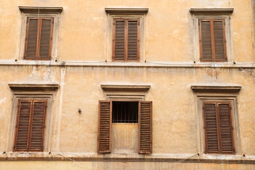 Shuttered windows in an old building, with the shutters closed on all windows but one. Horizontal shot.