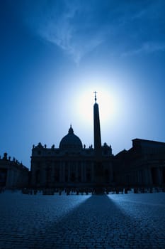 The east facade of St Peter's Basilica with the obelisk in the foreground. The sun is directly behind the obelisk. Vertical shot.
