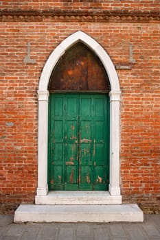 Weathered exterior doors in an arched doorway on a brick building in Venice, Italy. Vertical shot.
