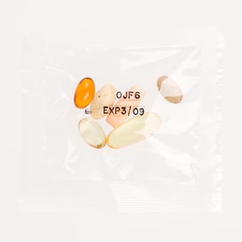 Pack of daily vitamin supplements in a clear plastic bag, stamped with an expiration date. Square format. Isolated on white.