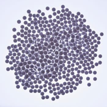 Purple tinted pile of round pills against white backlit background. Square format. Isolated on white.