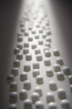 White round pills illuminated by a shaft of light. Vertical shot.