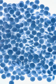 Blue toned pile of round pills backlit against a white background. Vertical shot. Isolated on white.
