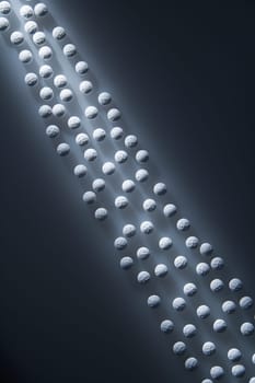 Overview of white round pills illuminated by a shaft of light. Vertical shot.