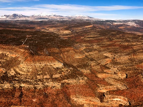 Aerial view of an arid, craggy landscape with mountains in the background. Horizontal shot.