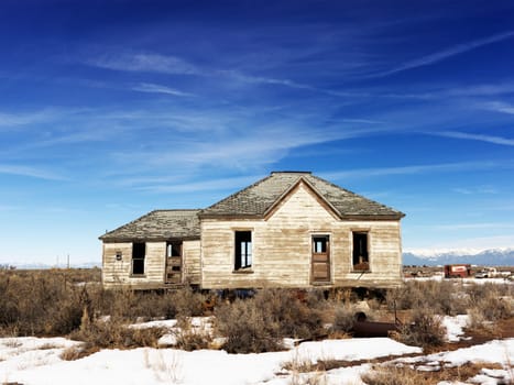 An abandoned home in the remote countryside. Snow and shrubs cover the ground. Horizontal shot.