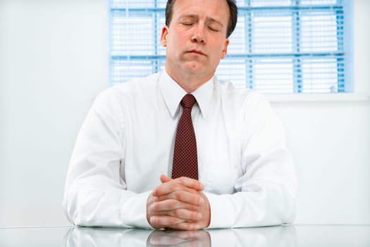 Caucasian middle aged businessman sitting at desk with eyes closed.