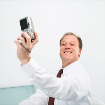 Caucasian middle aged businessman taking picture of himself with camera smiling.