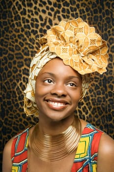 Close-up portrait of a smiling African American woman wearing traditional African clothing in front of a patterned wall. Vertical format.