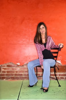 Attractive young adult woman sitting on a chair in front of a colorful wall. Vertical shot.