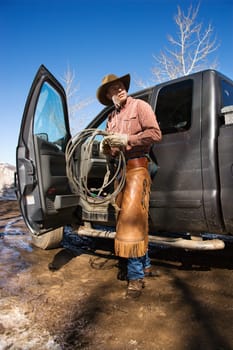 Man standing with a lariat next to the open door of a pickup truck. Vertical shot.