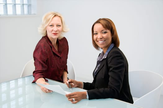Businesswomen sitting at office desk discussing paperwork.