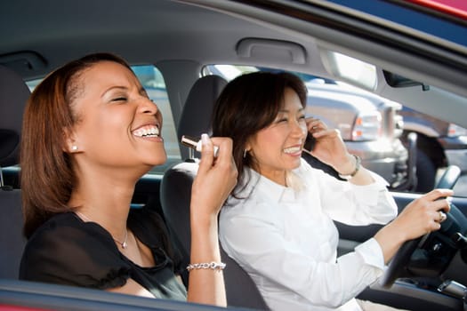 Women distracted and laughing in car with cellphone and cosmetics.