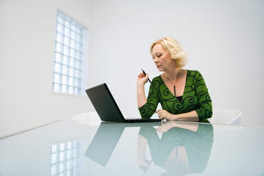 Caucasian middle aged businesswoman in office working on laptop computer.