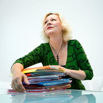 Caucasian middle aged businesswoman sitting at office desk with pile of folders.
