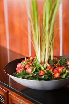 Selective focus close-up of a floral decoration consisting of primroses and greenery in a black bowl. The bowl is sitting on a piece of furniture. Vertical shot.