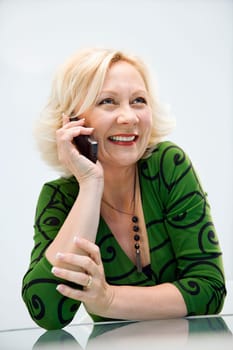 Caucasian middle aged businesswoman in office on cellphone smiling.