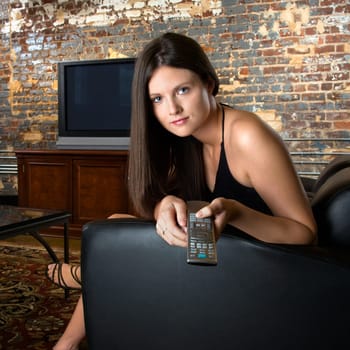 Pretty Caucasian young woman sitting in chair pointing remote control and pushing button.