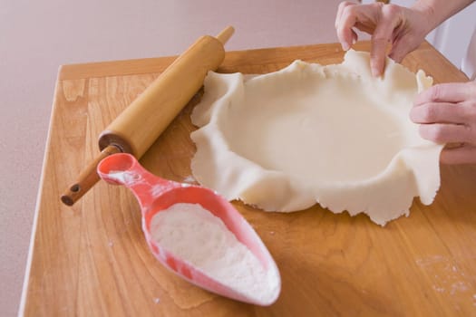 covering pie pan with dough on a cutting board with rolling pin and flour