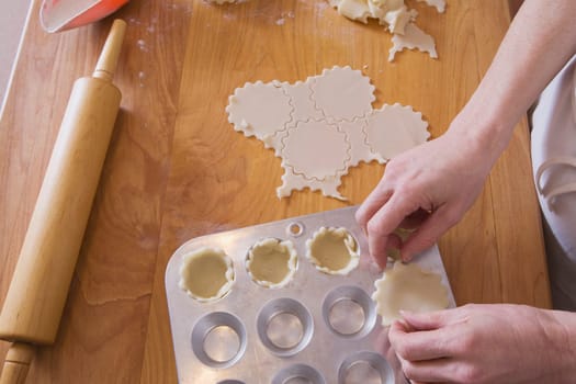 person placing dough into muffin pan on cutting board with rolling pin