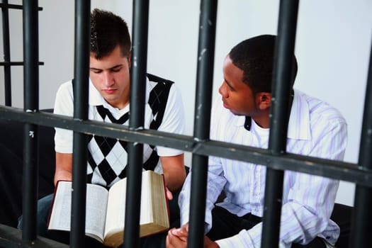 a young man reads the bible to another young man in jail