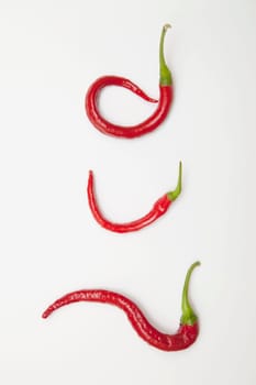 three red jalapeno peppers curled into unique shapes