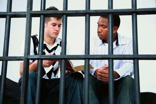 a young man reads the bible to another young man in jail