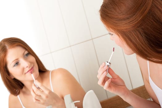 Body care - young woman apply lip gloss