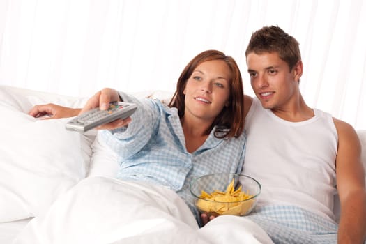 Couple lying in bed watching television
