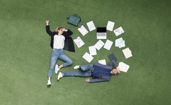 Top view of coworkers lay tired on grass, exhausted employees surrounded with papers, business documentation. Sleepy, overworked, stressed, enough concept