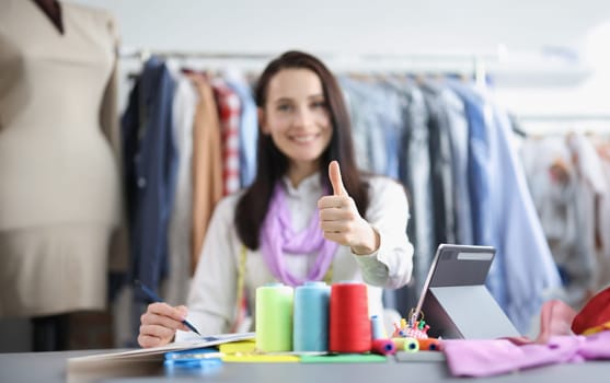 Portrait of positive female seamstress in atelier, thumbs up gesture, talented dressmaker. Smiling designer owns successful atelier. Sew, fashion concept