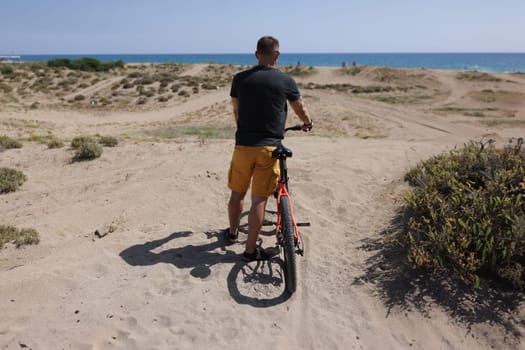 Portrait of person stand with back, arriving at his destination after bike ride to rest on beach. Nature, hobby, holiday, sport, physical activity concept