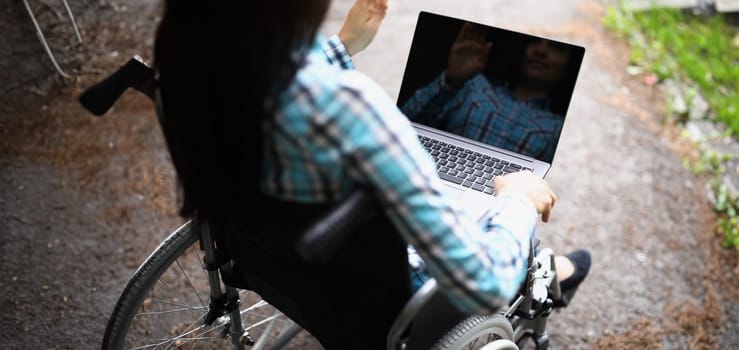Close-up of woman in wheelchair wave hello on video call, laptop for remote work. Computer with black screen, Technology, disabled people, mockup concept