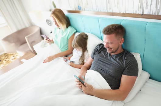 Close-up of family stare in smartphone, morning in bed with devices, kill time. People addicted to modern technologies, bored. Social media, addict concept