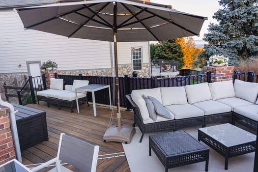 Morning on a summer day. Fully furnished backyard patio with a grill, sitting area, and umbrella.