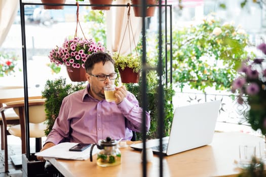 man works in a restaurant remotely with a laptop and drinks tea