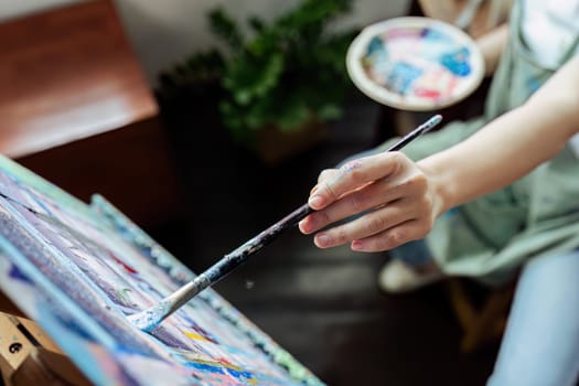 Female artist hold color palette and paintbrush for painting during hobby workshop.