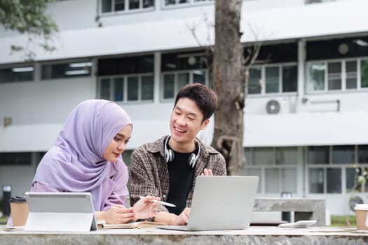 Young students of different nationalities are tutoring or doing homework together on a bench on campus..