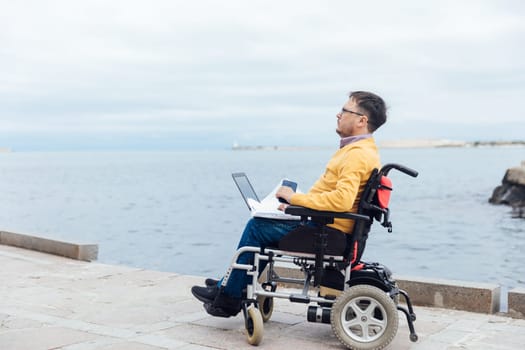 a man on a walk by the sea with a laptop looks into the distance