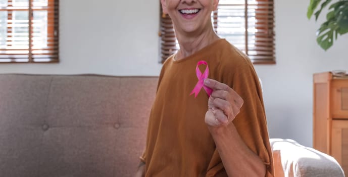 Close-up elderly senior woman with pink ribbon at her home. Health care, support, prevention. Breast cancer awareness month concept.