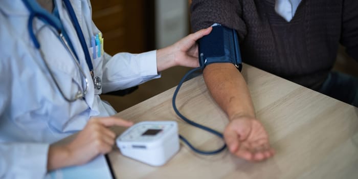 nurse doctor using digital tonometer check blood pressure for old asia female at home in elderly care cardiovascular medical visit, cholesterol problem. Home health care and nursing home concept.