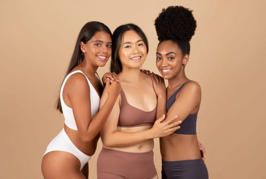 Three multiracial women exude natural beauty while posing in underwear, offering refreshing, authentic and harmonious image on beige studio background