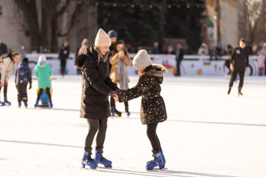 Action shot of beautiful woman teaching her daughter how to ice skate.