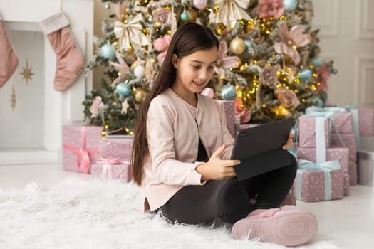 Cute girl using computer by christmas tree.